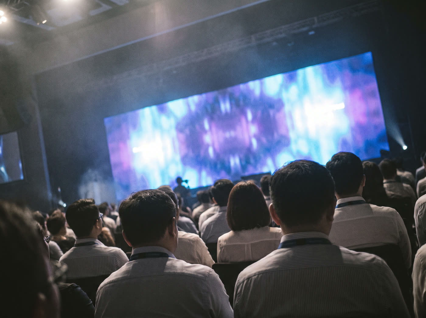 A large conference hall mid-keynote, audience lit in blue